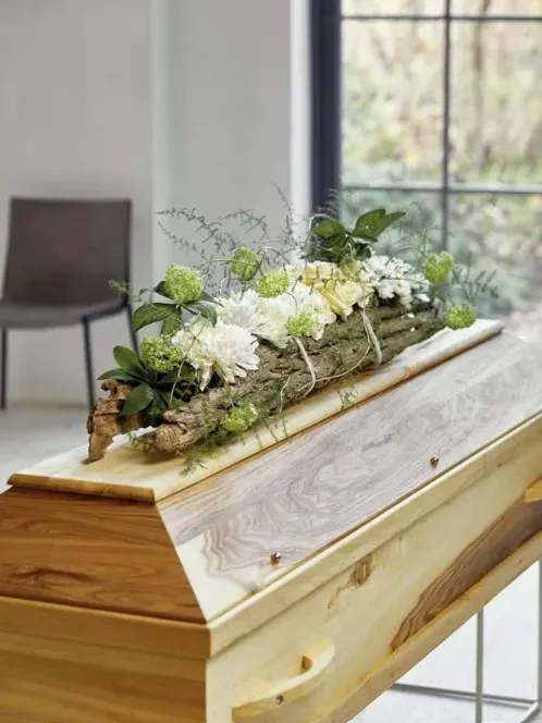 Cercueil en bois clair orné d'une composition florale naturelle et champêtre.